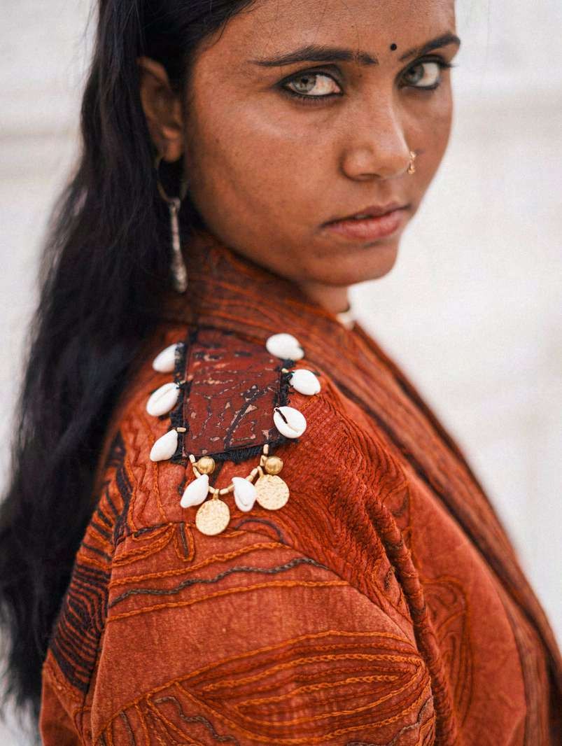 A woman wearing a rust-toned ritual coat with cowrie-shell and coin adornment